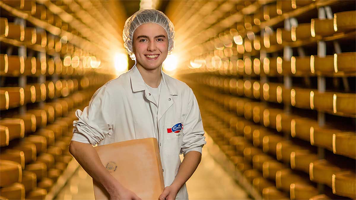 Ein Milchtechnologe im Käsekeller hält einen quadratischen Käse in der Hand