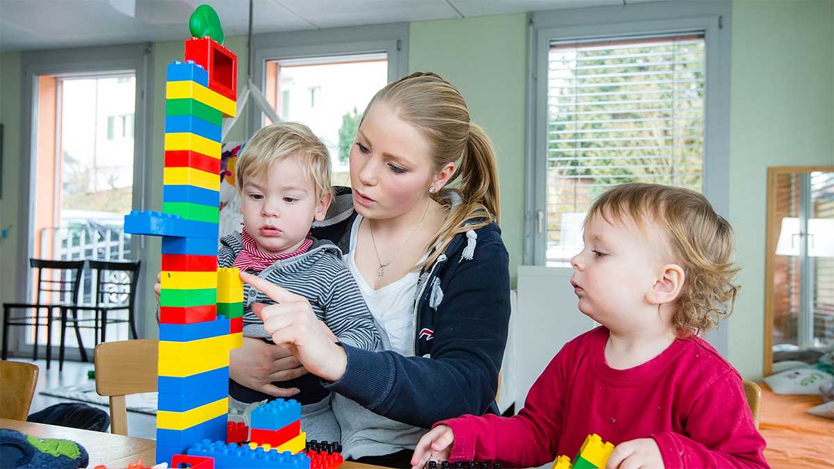 Eine Fachfrau Betreuung spielt mit zwei kleinen Kindern Lego Duplo